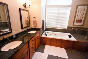 A bathroom with two sinks, a bathtub, wooden cabinets, a mirror, and a window with blinds. - Cozy 2-bedroom condo in wonderful Emmetsburg (Emmetsburg)