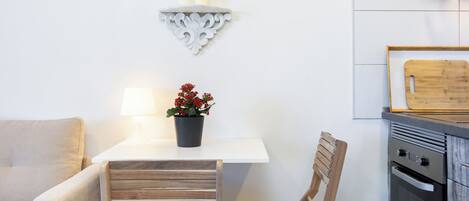 A modern kitchen with a white countertop, wooden chairs, a small table with a potted plant, and a wall-mounted shelf with candles.