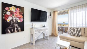 Ein Wohnzimmer mit Fernseher, einer Couch, einem Couchtisch und einem Bild an der Wand.