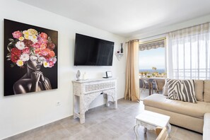 Ein Wohnzimmer mit Fernseher, einer Couch, einem Couchtisch und einem Bild an der Wand.