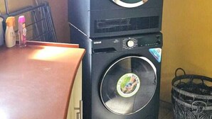 Una lavadora y secadora apiladas en una habitación con piso de baldosas y pared marrón.