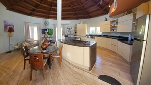 Una cocina moderna con una isla central, un comedor con una mesa redonda y una sala de estar con sofá.