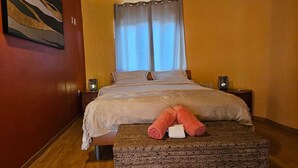Habitación de hotel con cama, dos mesitas de noche, aire acondicionado instalado en la pared, ventana con cortinas y un cuadro en la pared.