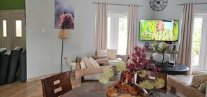 Een woonkamer met een bank, een televisie, een klok en een vaas met bloemen.