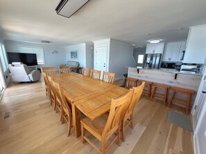 Un salón comedor amplio con una gran mesa de madera, asientos cómodos, un televisor de pantalla plana y una cocina equipada con electrodomésticos modernos.