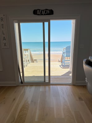 A room with a large sliding glass door leading to a beach view, a wooden deck, and a sign that reads 'BEACH'. - Oceanfront Luxury Retreat  5BR Sleeps 18  Newly Renovated (North Topsail Beach)