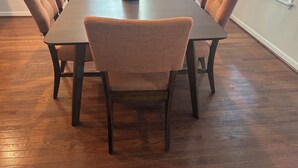 A dining table with six chairs, a tissue roll, and a window with blinds.