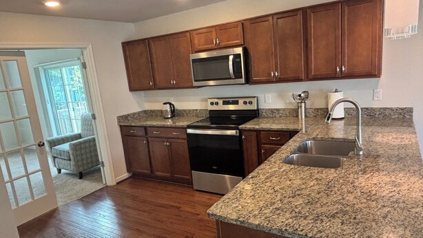 A kitchen with wooden cabinets, a stainless steel microwave, an oven, a granite countertop, and a sink.