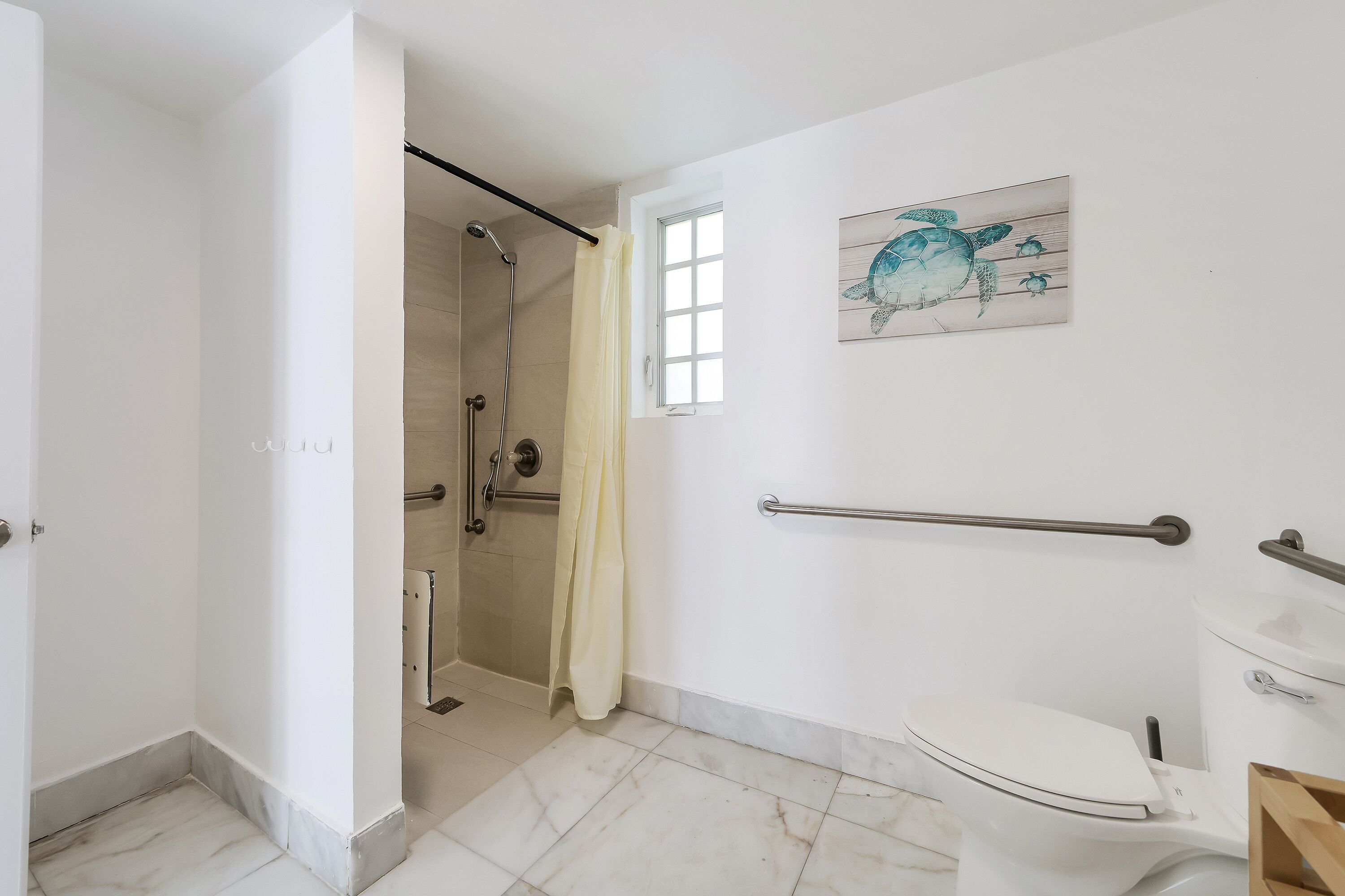 Un bagno con il water, una doccia, un corrimano e una finestra.