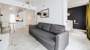 A living room with a grey sofa, a dining table with chairs, a kitchen area, and a black wall with a mirror. - Alton Apts by At Mine Hospitality (Miami Beach)