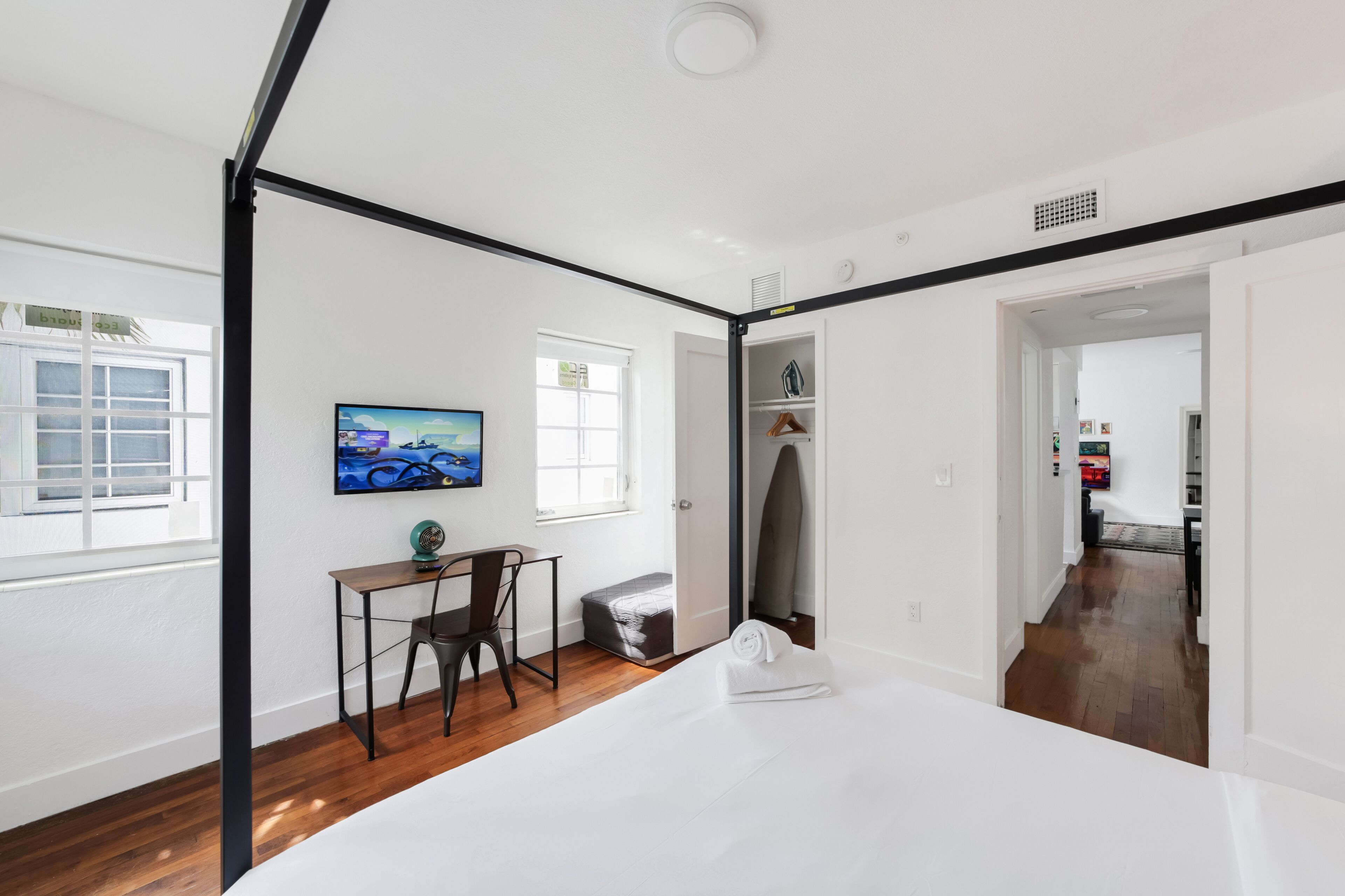 Habitación de hotel moderna con cama, escritorio, silla, televisión y vista al pasillo.