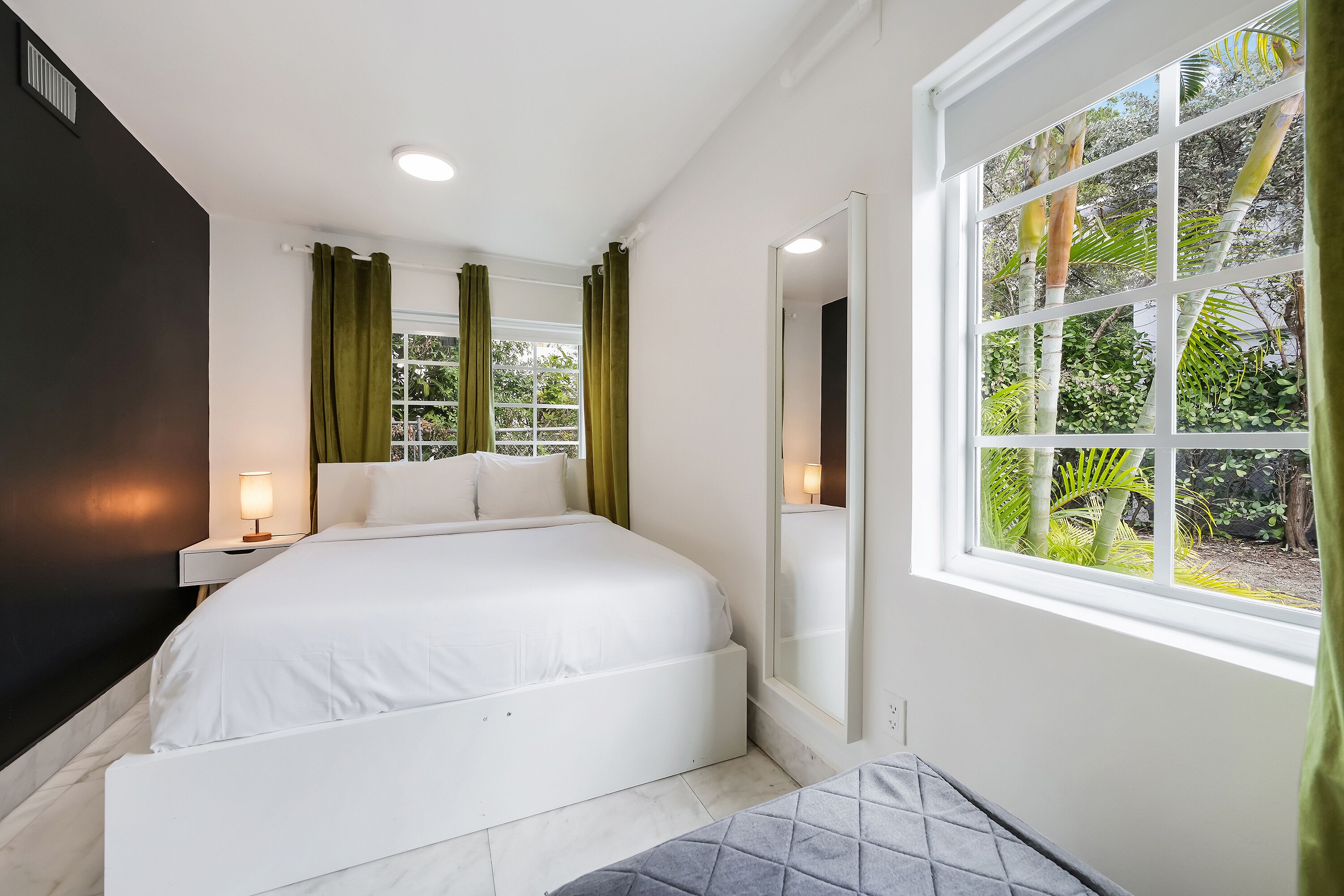 A bedroom with a bed, a nightstand, a window with curtains, and a view of greenery outside.