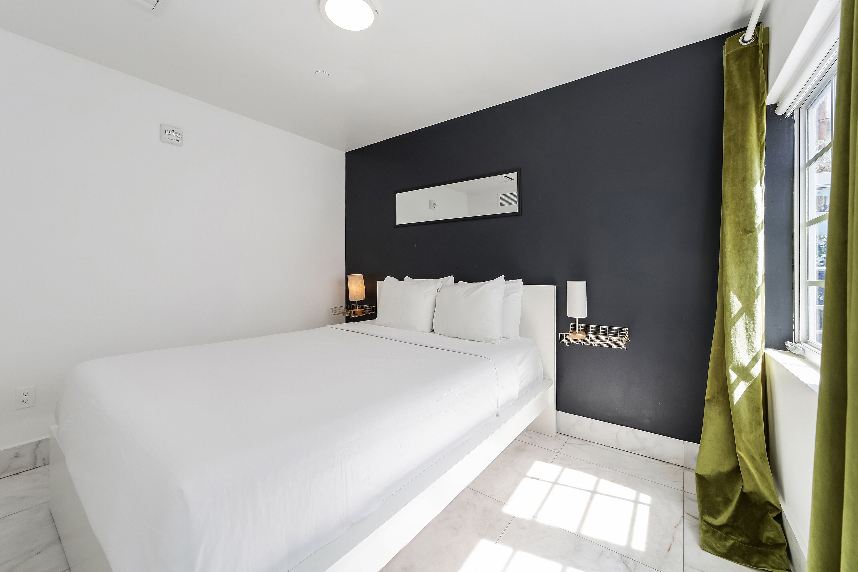 Een moderne hotelkamer met een groot bed, een nachtkastje met lamp, een spiegel en een raam met gordijnen.