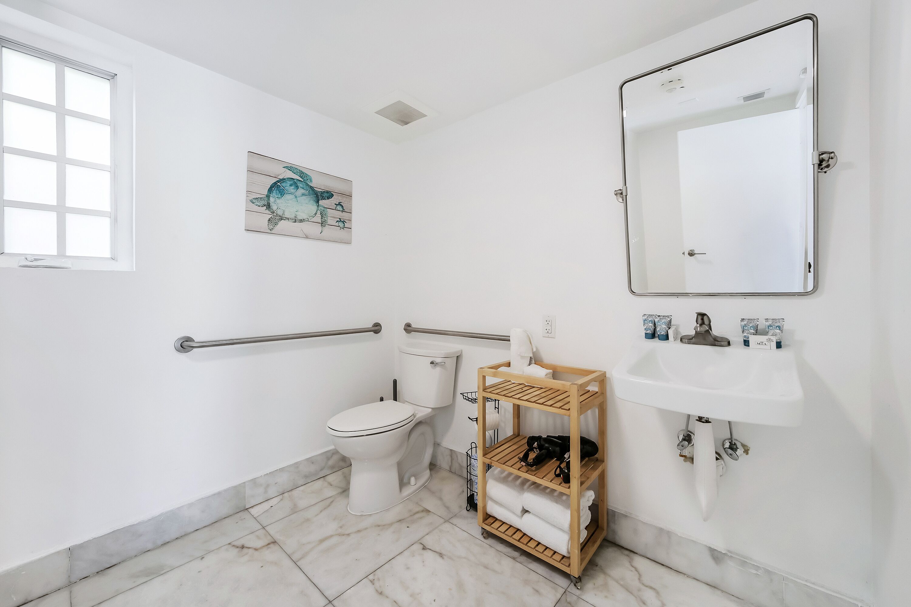 Un baño con inodoro, lavamanos, espejo, ventana y toallero.
