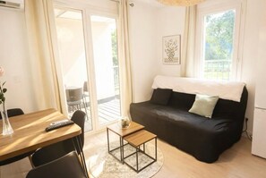 A living room with a black sofa, a small wooden table, a glass vase, and a remote control on a wooden table. - Apartment 78, Résidence Les hameaux de Saint-Cyprien, 5 minutes from the beach. (Lecci)