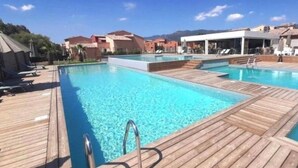 Ett poolområde med trädäck, solstolar och en överbyggd sittplats.