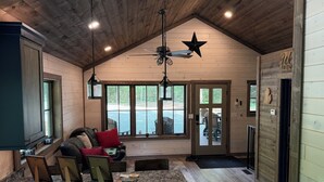 A cozy cabin-style interior with a wooden ceiling, a ceiling fan, a large window, a built-in bench, and a kitchen counter.