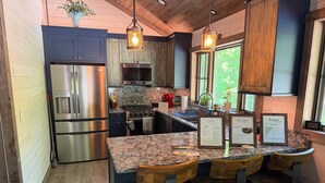 A modern kitchen with stainless steel appliances, a granite countertop, and wooden bar stools.