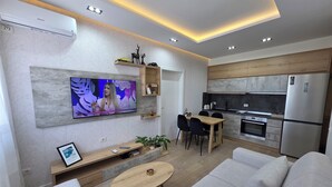 En moderne stue med TV, sofa, spisebord og et køkkenområde.