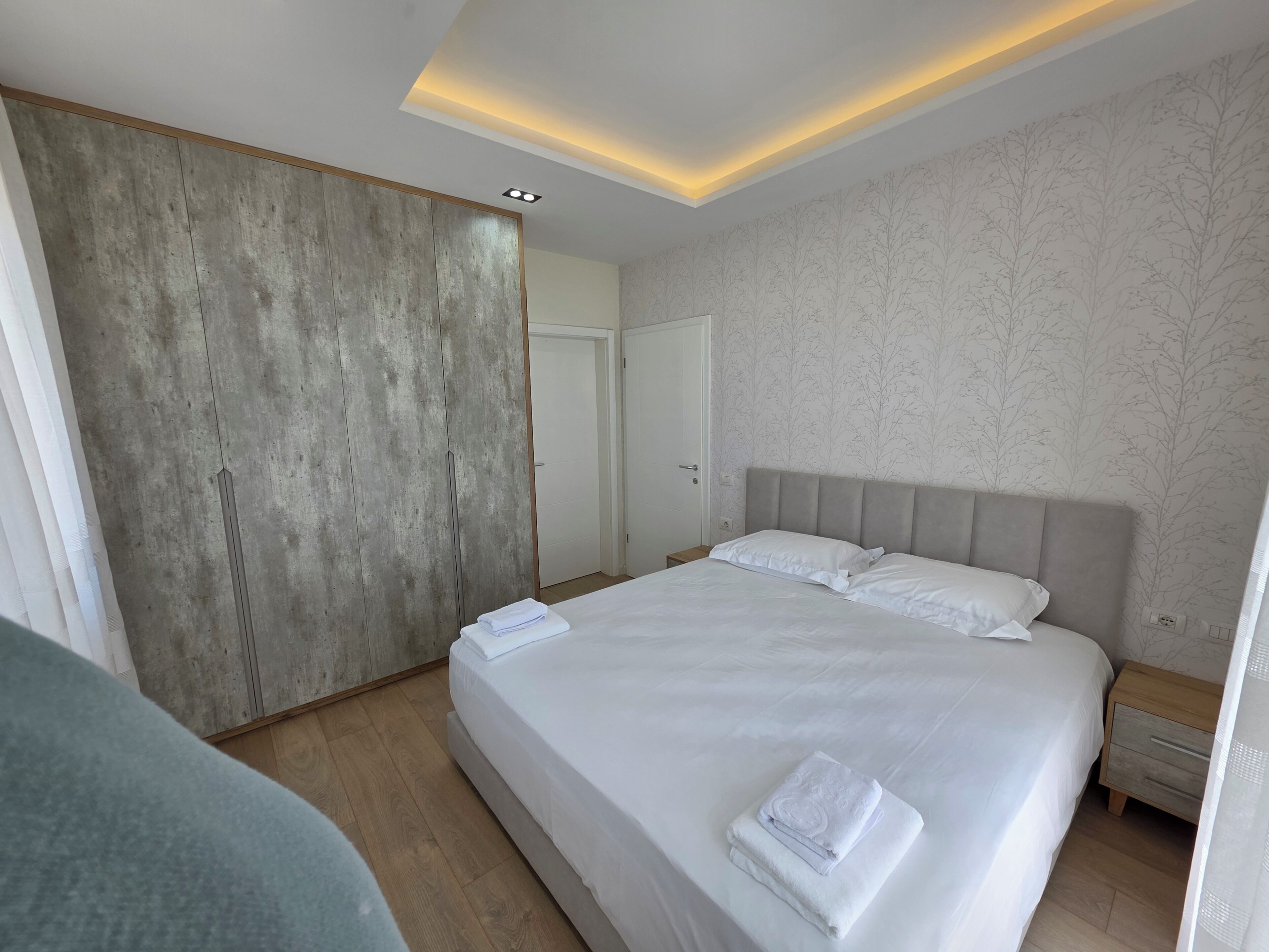 A modern hotel room with a large bed, a wooden wardrobe, and a patterned wall.