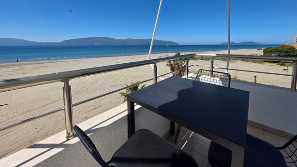 En balkon med bord og stole med udsigt over en strand og havet.