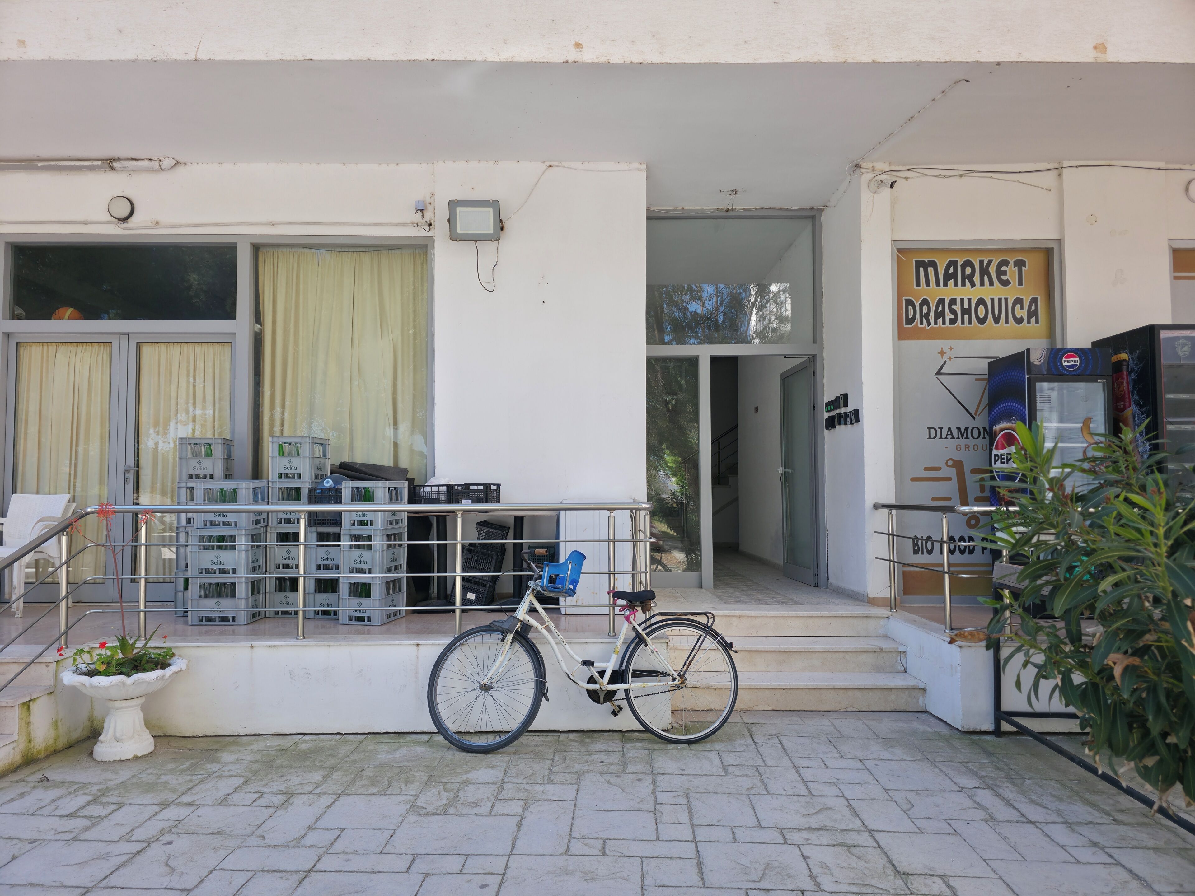 L'ingresso di un edificio con una bicicletta parcheggiata fuori, una scala che conduce all'ingresso e una macchina distributrice a destra.