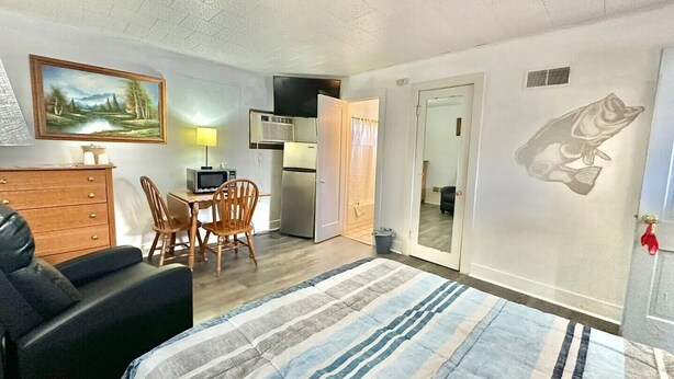 A bedroom with a bed, a desk with a chair, a kitchenette, and a door with a fish decal. - Flora Motel (Flora)
