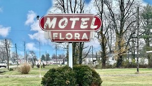 A motel sign with the name 'Motel Flora' in a rural setting with trees and a clear sky. - Flora Motel (Flora)