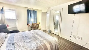 A hotel room with a bed, a desk, a chair, a TV, and a door. - Flora Motel (Flora)
