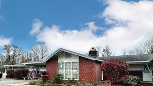 A single-story brick house with a front porch, a chimney, and a large window. - Flora Motel (Flora)