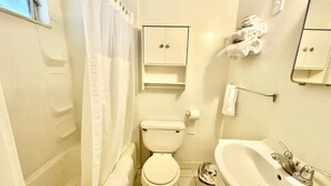 A small, compact bathroom with a toilet, sink, and a shower curtain. - Flora Motel (Flora)