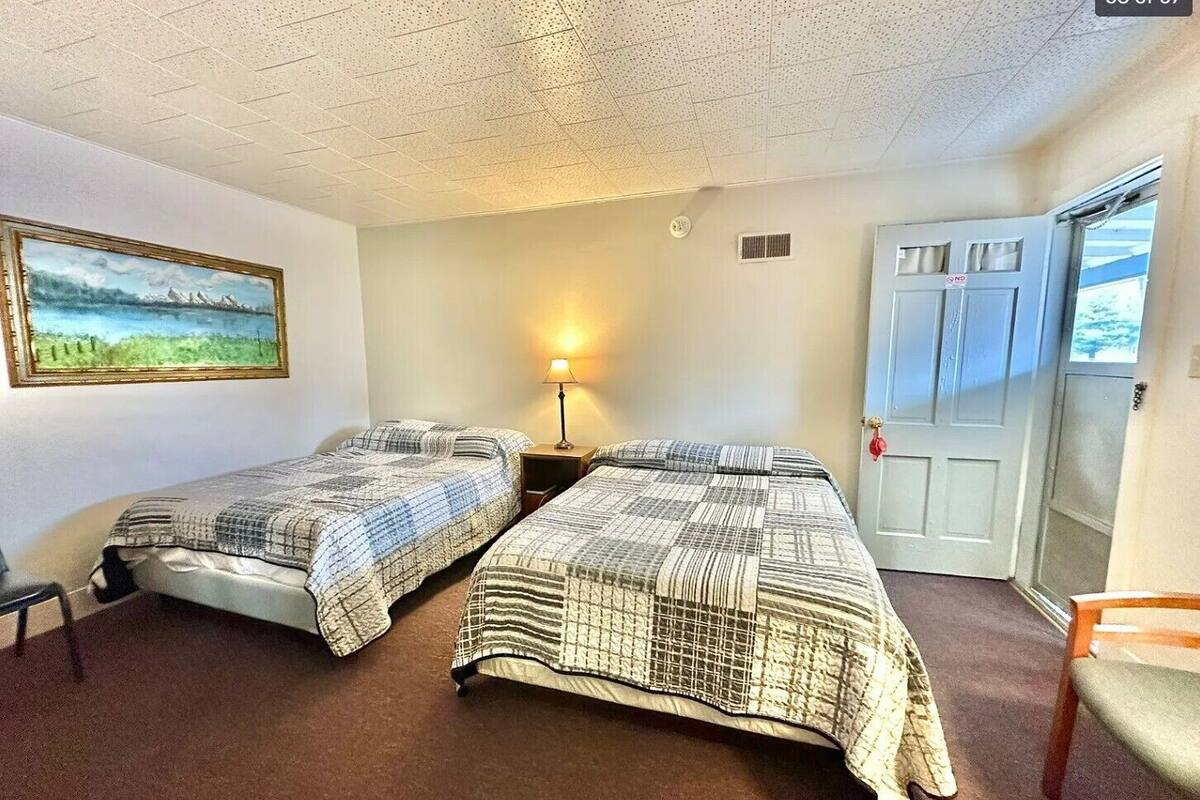 A room with two beds, a painting, a lamp, a door, and a chair.