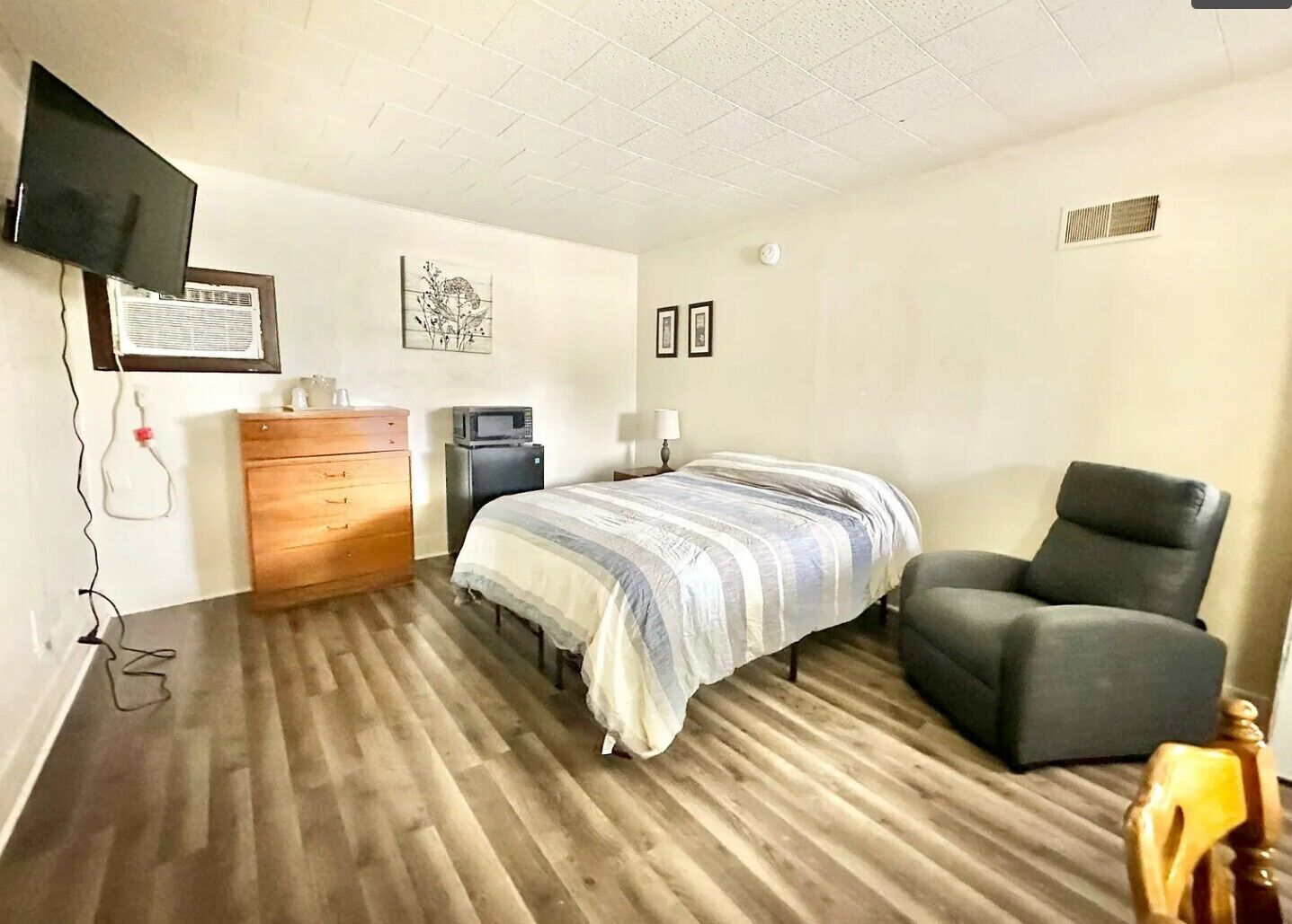 Un dormitorio con cama, una silla, cómoda, televisor y microondas.