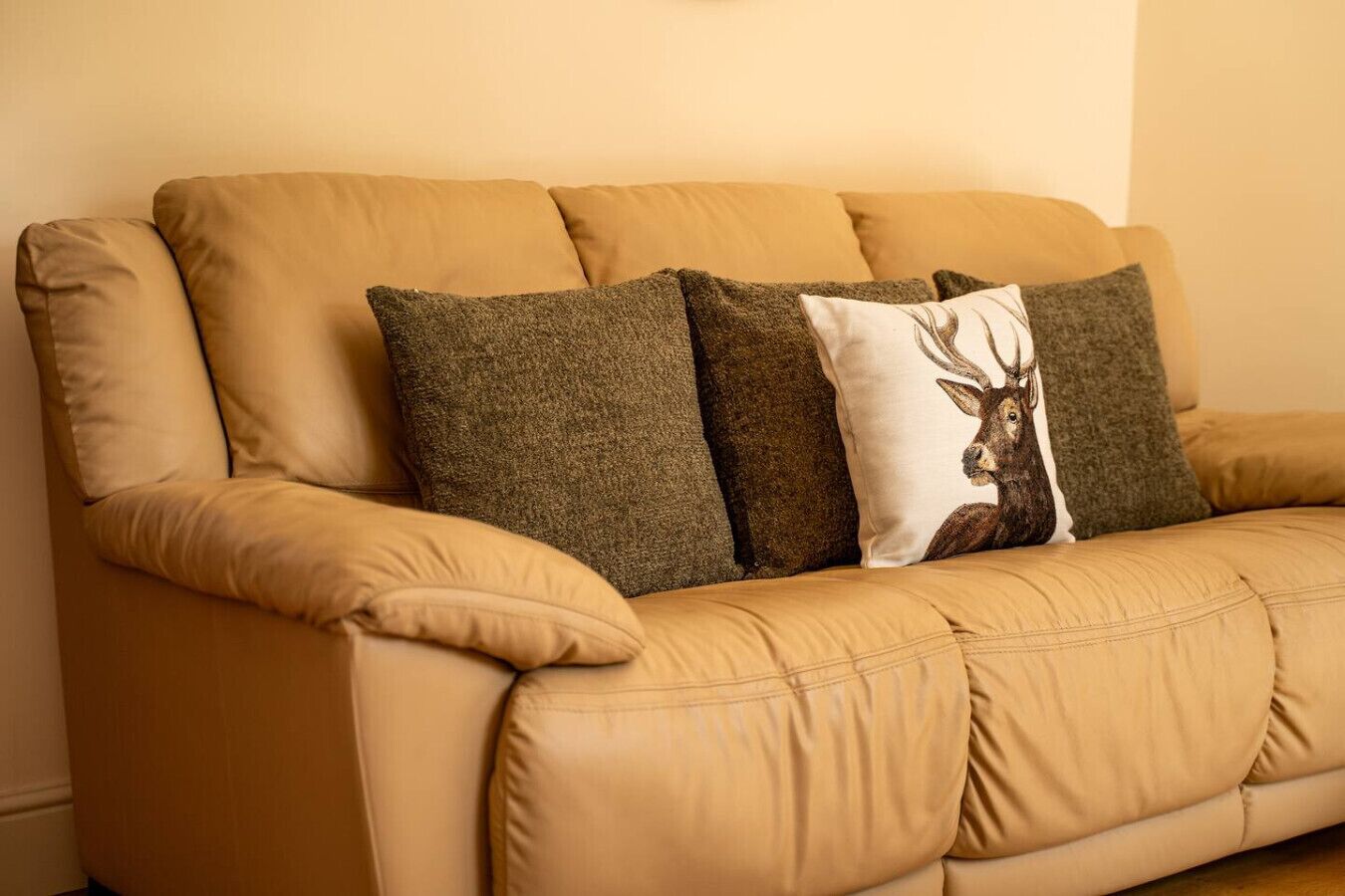 Un canapé en cuir beige avec trois coussins, dont l’un est orné d’un motif représentant un cerf.