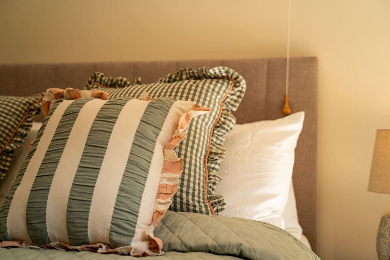 A bed with striped pillows and a quilted cover.