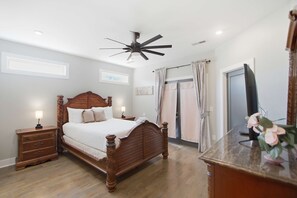 Ein Schlafzimmer mit einem hölzernen Himmelbett, einem Deckenventilator, einem Nachttisch mit Lampe, einer Kommode und einem Spiegel.