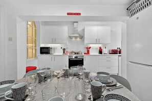 Een moderne keuken met witte kasten, een magnetron en een spoelbak. Er staat een eettafel gedekt met glazen en borden.