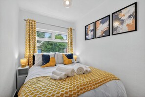 Een hotelkamer met een bed, gordijnen, een raam en twee ingelijste kunstwerken aan de muur.