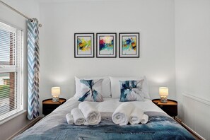 A hotel room with a bed, two bedside tables with lamps, a window with blinds, and three abstract paintings on the wall. - SuperHost Long Stays, Parking, Garden, Fast Wifi. (Lisburn and Castlereagh)