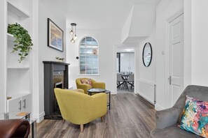 Een moderne woonkamer met een open haard, een geel fauteuil, een grijze bank en een eethoek op de achtergrond.