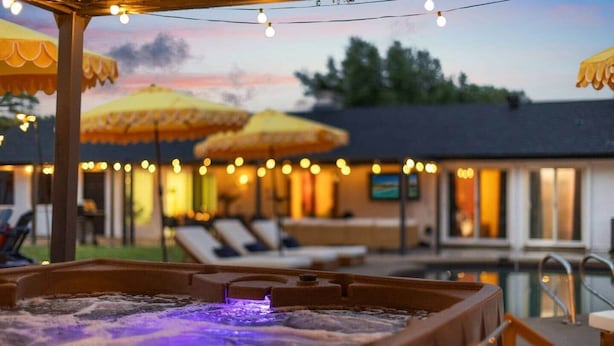 Un bain à remous avec un éclairage violet, des parasols pour l’extérieur et un espace aménagé au bord de la piscine avec des chaises longues.