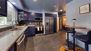 Une cuisine moderne avec des meubles de couleur sombre, des appareils en acier inoxydable et un coin repas comprenant une table et des chaises.