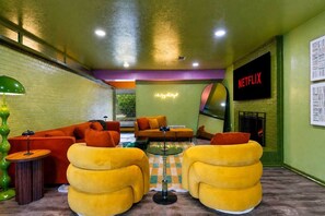 A modern living room with orange and yellow sofas, a fireplace, a Netflix sign, and a brick wall. - Kaleo - Pickleball | Pool | Hot Tub | Central Spot (Irving)