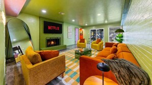 Un espace de détente moderne doté d’une cheminée, de canapés, de fauteuils et d’un grand écran de télévision affichant le logo « NETFLIX ».