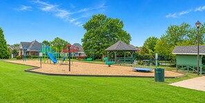 Ein Spielplatz mit Rutschen und Schaukeln, umgeben von einem gepflegten Rasen und Bäumen.