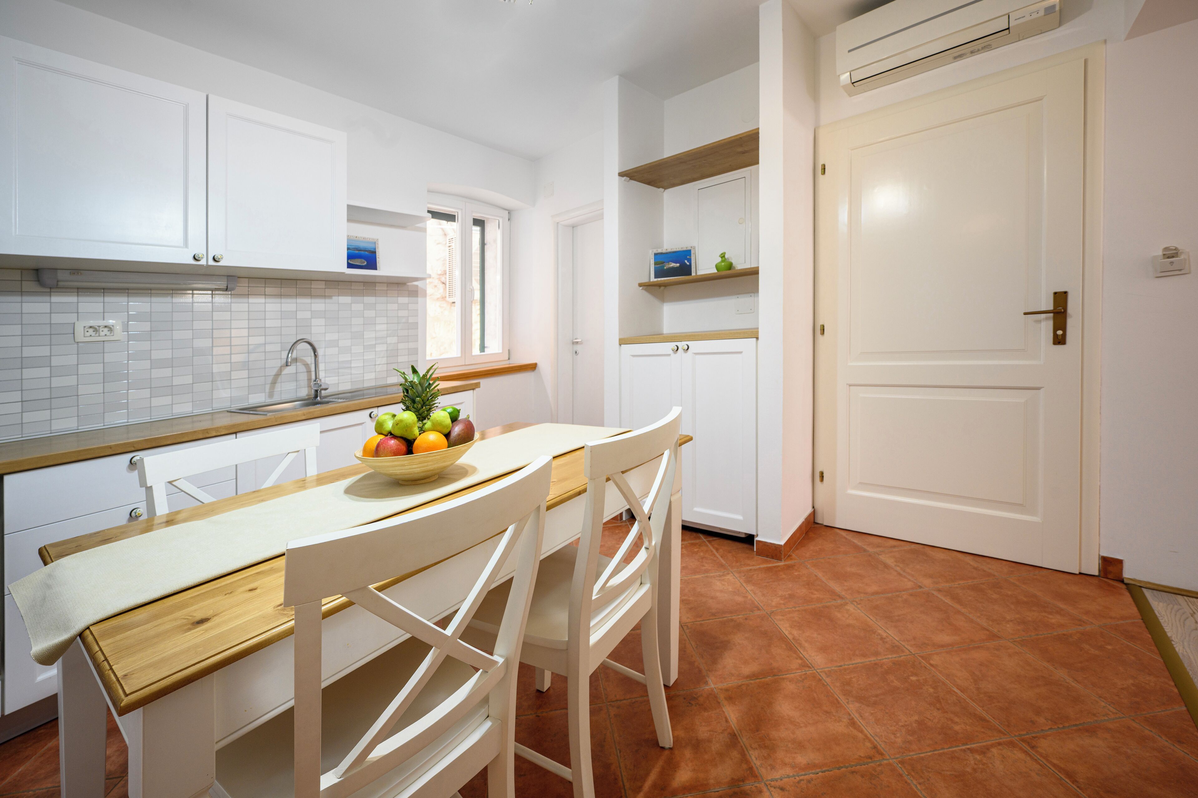 A kitchen with white cabinets, a wooden countertop, and a bowl of fruit.