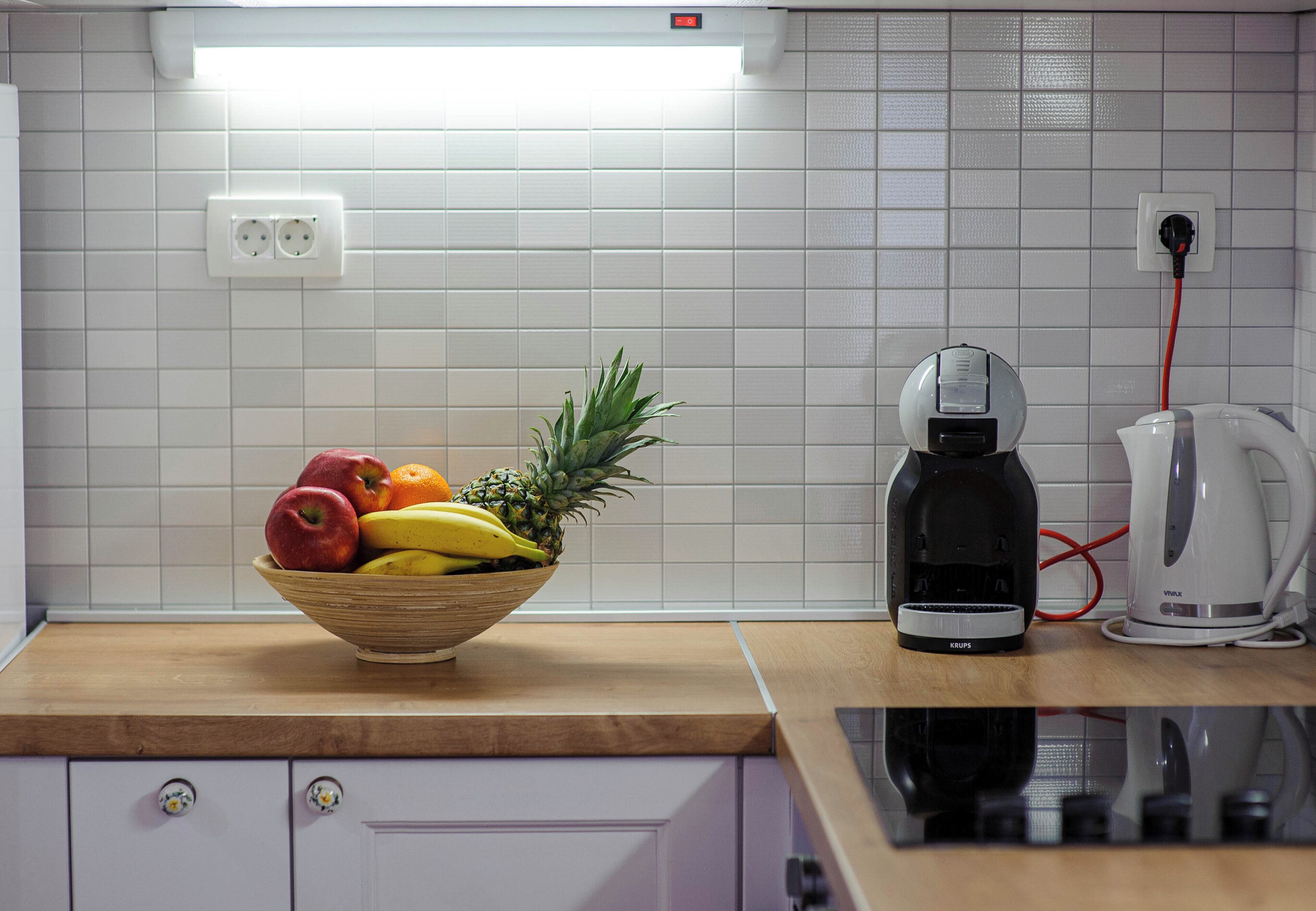 A kitchen with a fruit bowl, a coffee maker, and a kettle on the counter.