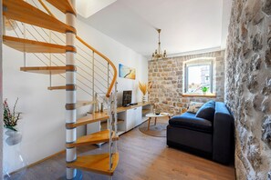 A modern living room with a wooden spiral staircase, a stone wall, a black sofa, and a small table with a plant.