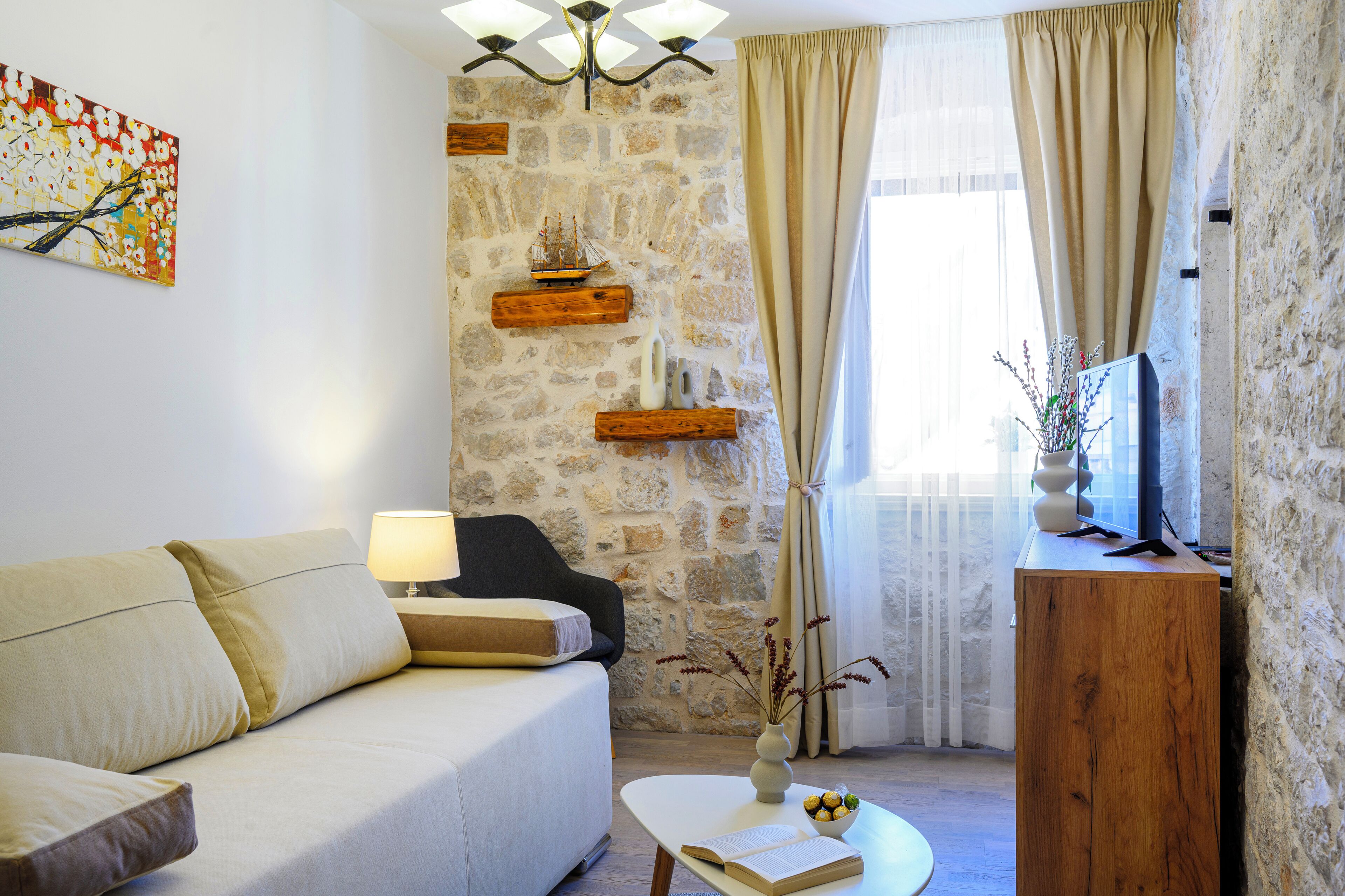 A living room with a stone wall, a sofa, a coffee table, a lamp, a ship model, and a TV.