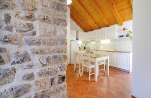A kitchen with white cabinets, a wooden ceiling, and a stone wall.